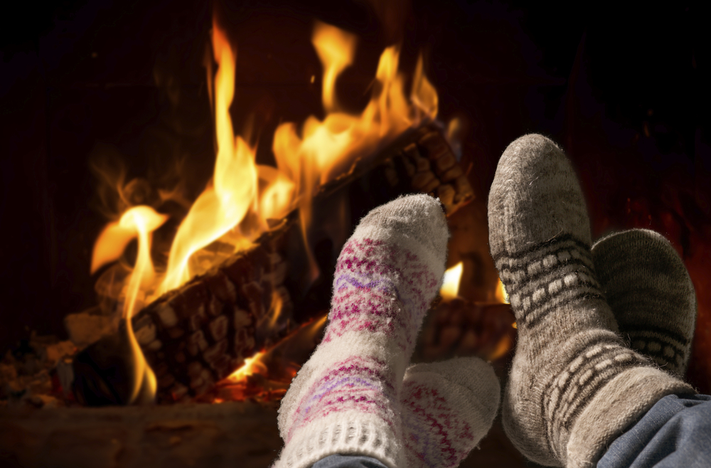Two pair of feet with wool socks in front of the fireplace